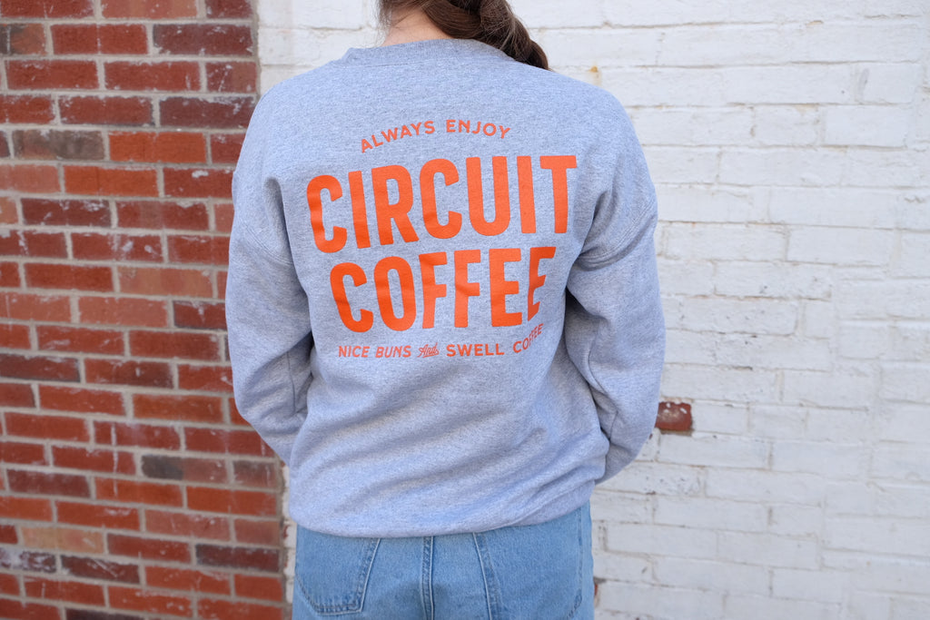 Person wearing a gray sweatshirt with 'Circuit Coffee' text against a brick wall.