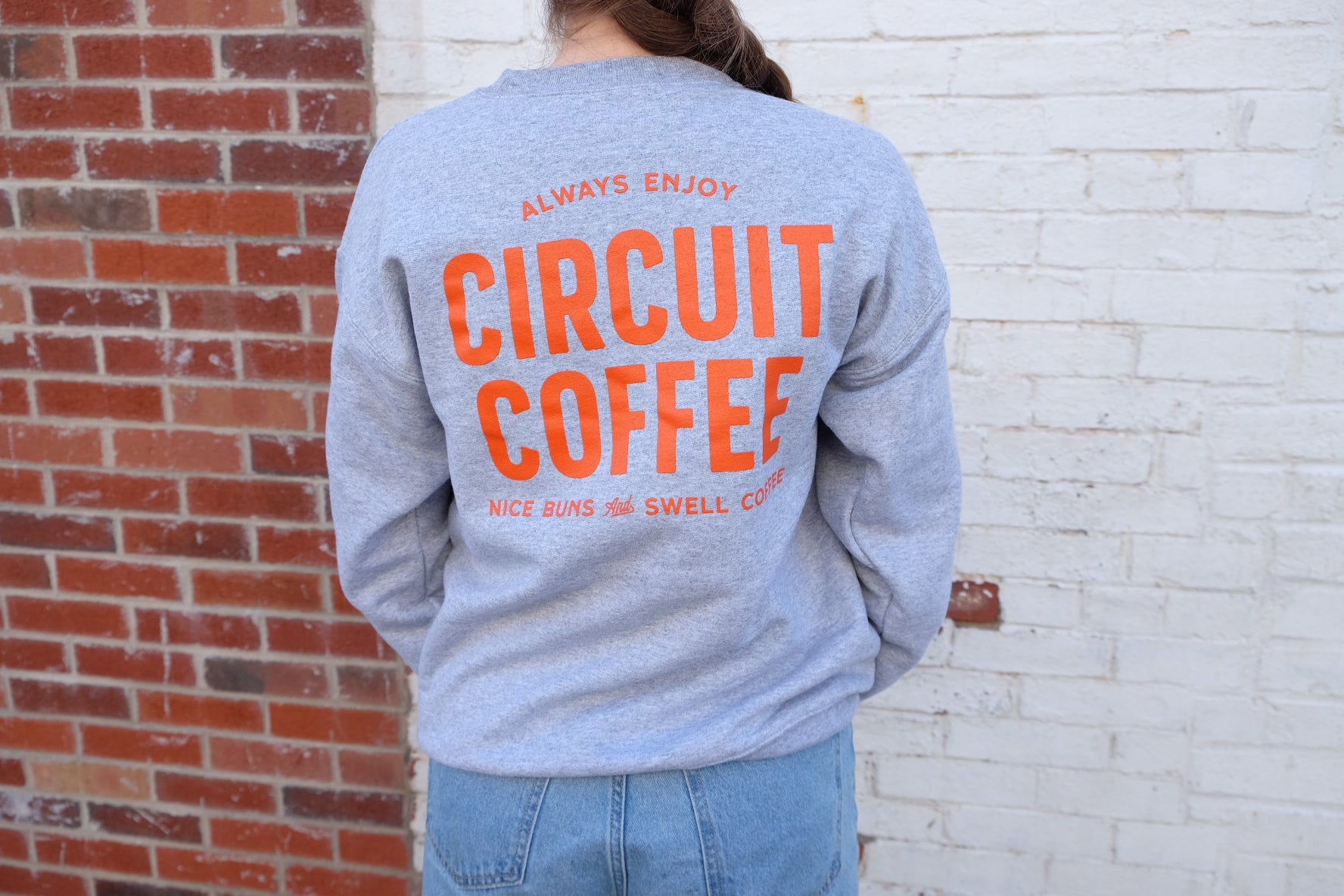 Person wearing a gray sweatshirt with 'Circuit Coffee' text against a brick wall.